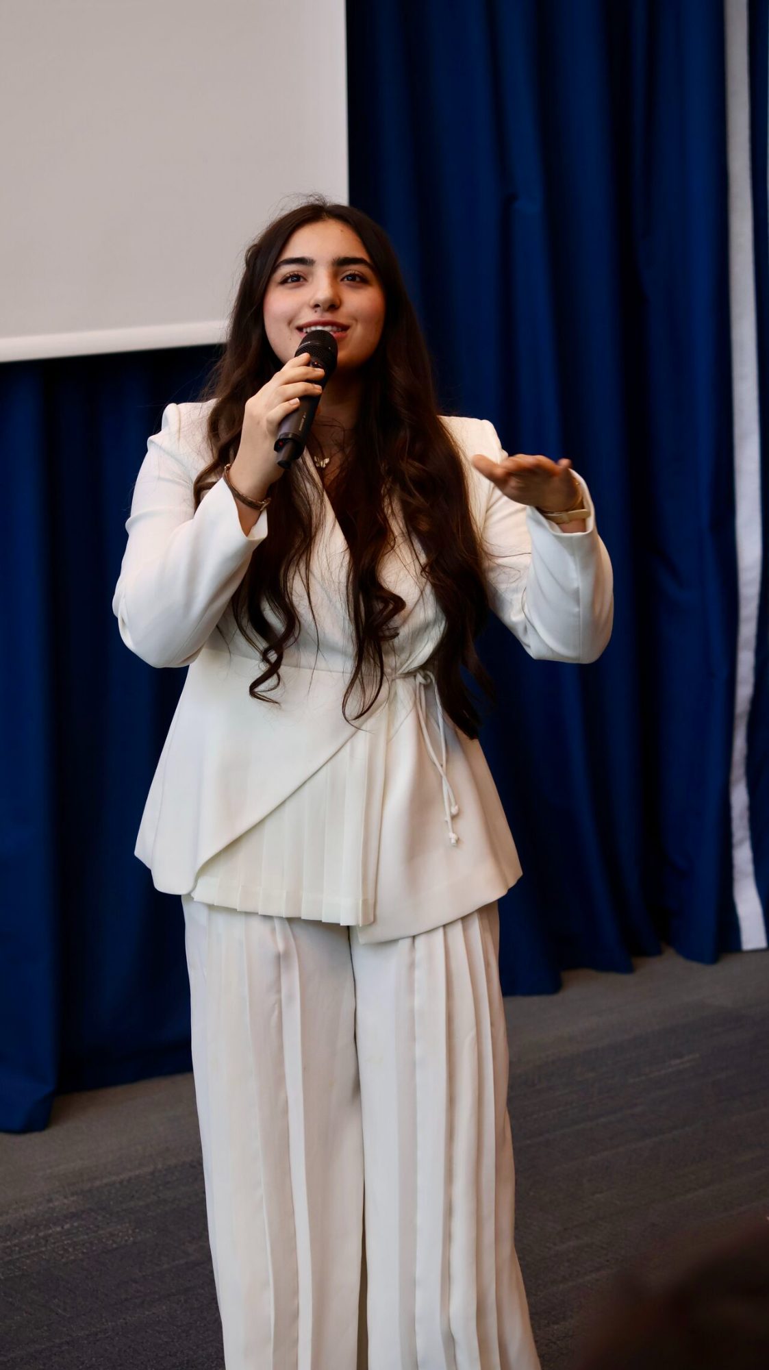 Student presenting with a microphone in front of a blue curtain